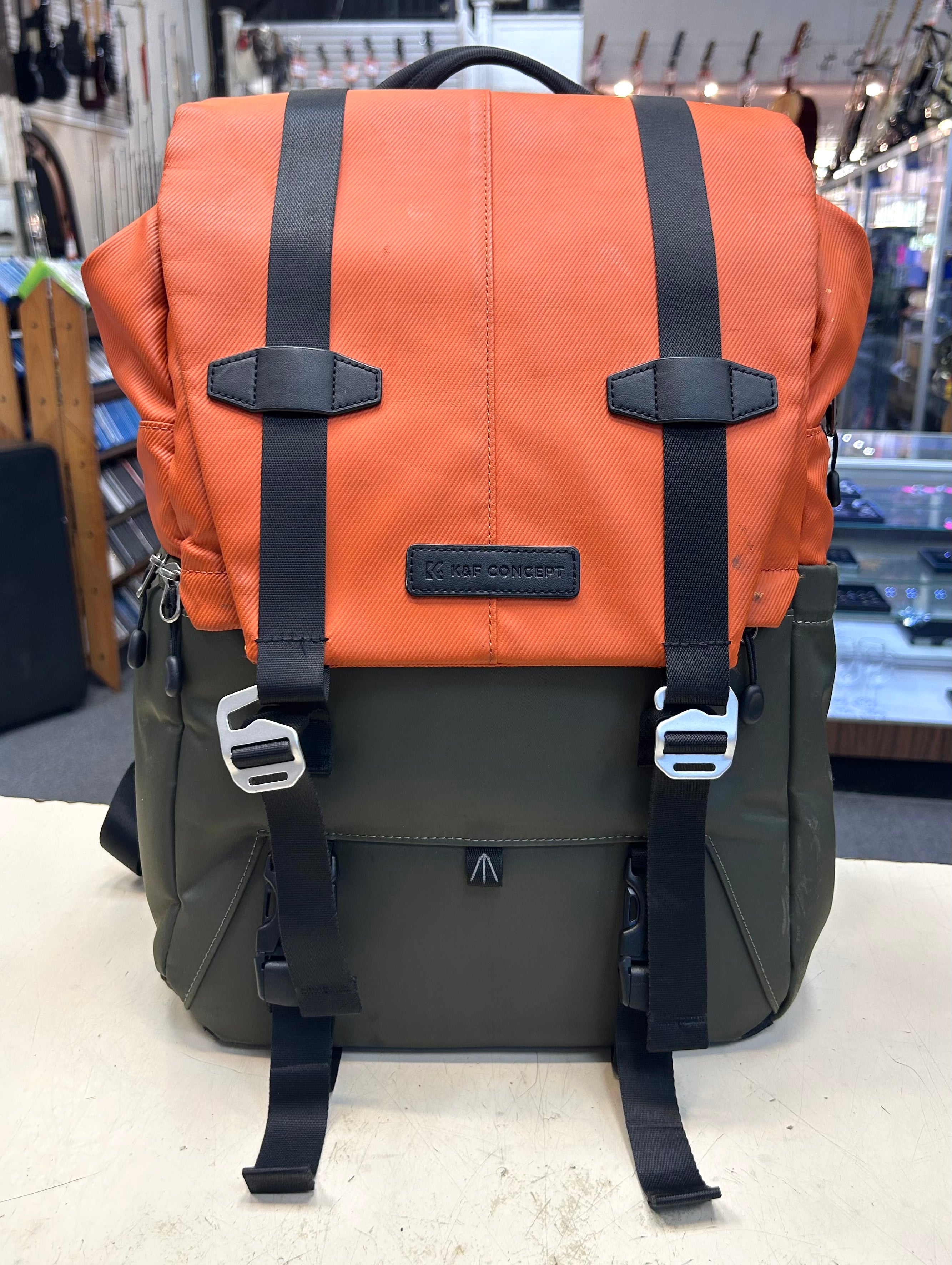 Two-tone camera backpack with orange top section and green bottom section on a light gray surface.