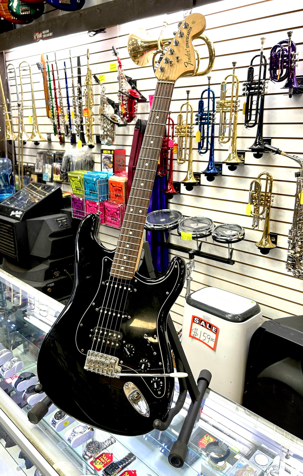 Black electric fender guitar on display in a music store with instruments in the background