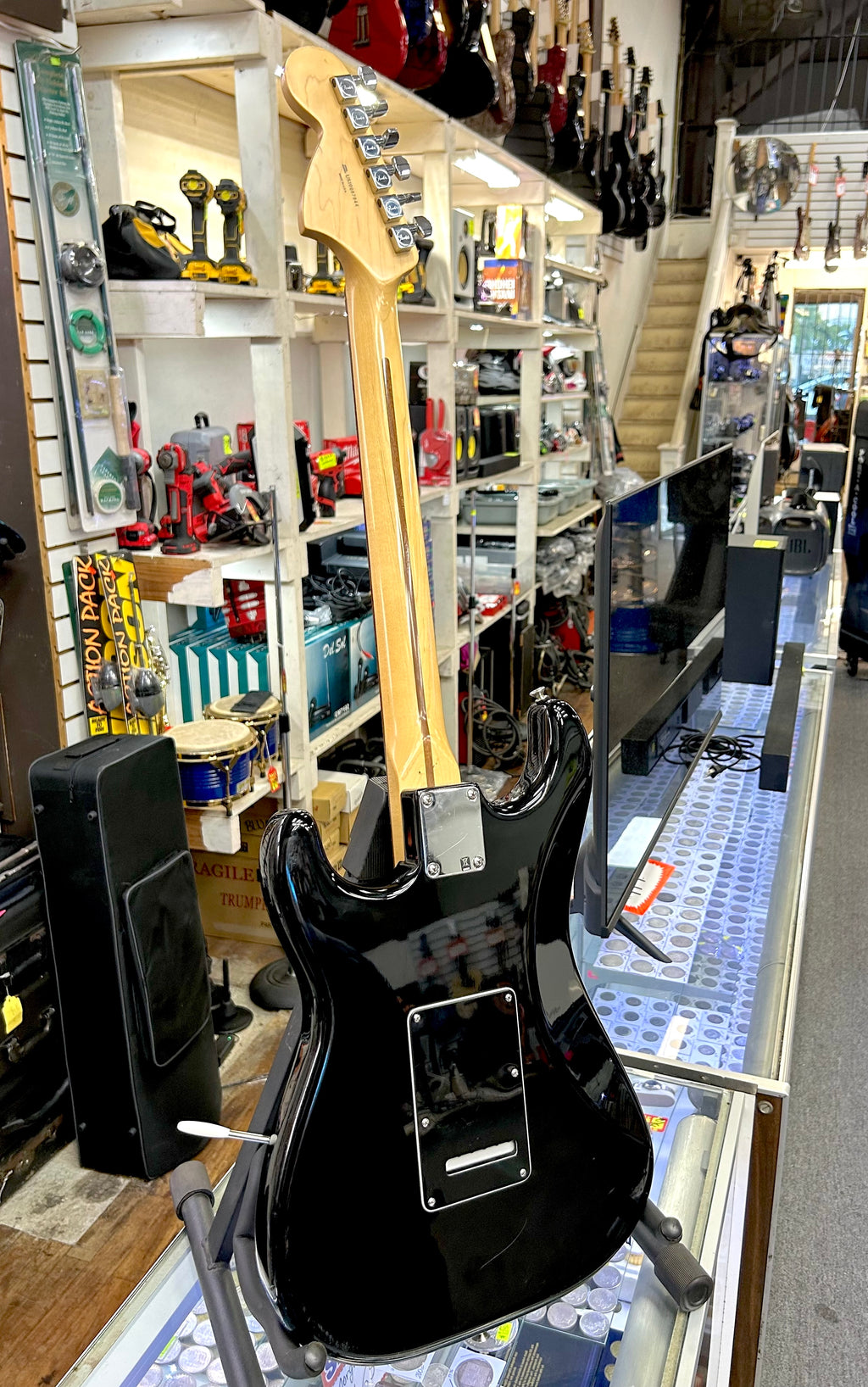 Black electric fender guitar on display in a music store with shelves and equipment in the background