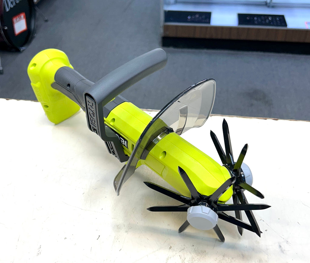 Green and black tool with circular blade and propeller-like attachments on a white surface.