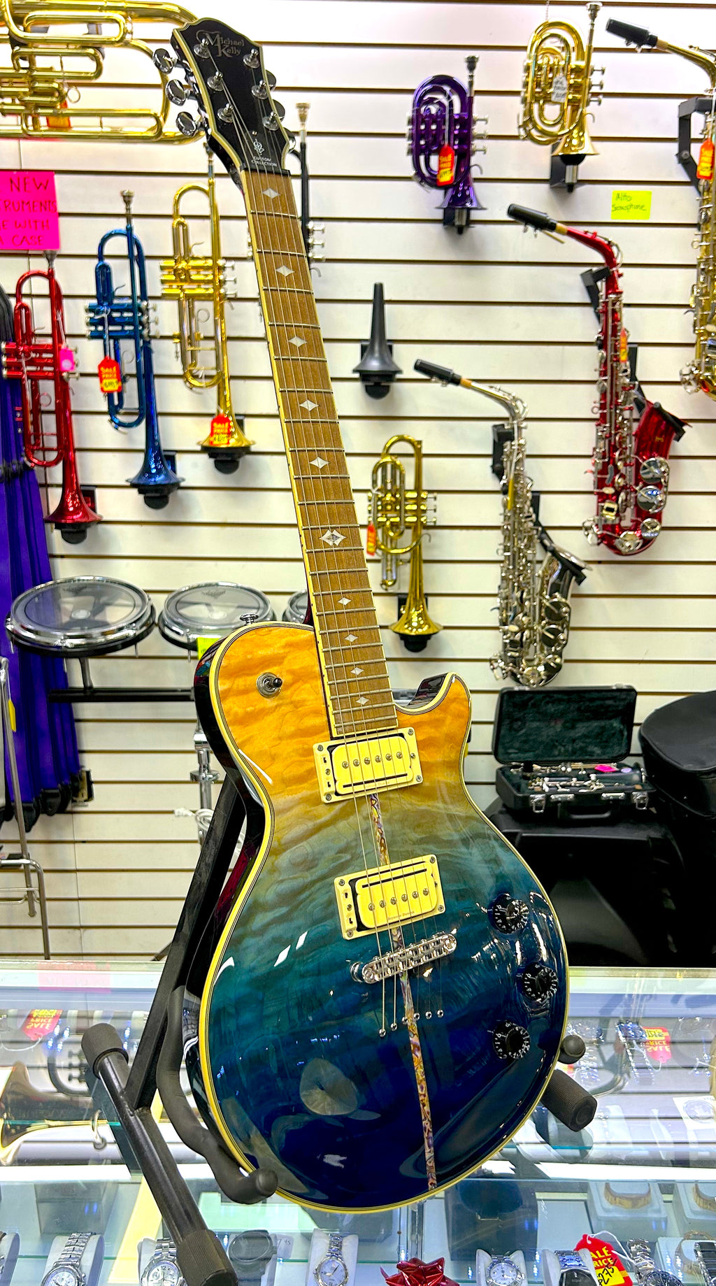 Michael kelly Blue electric guitar on display with musical instruments in the background