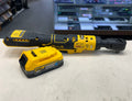 Yellow and black power tool with battery on a light surface, blurred electronic equipment in the background