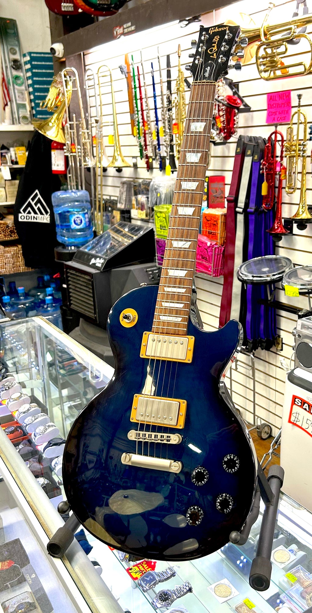 Blue electric guitar on display in a music store with various instruments and equipment in the background.