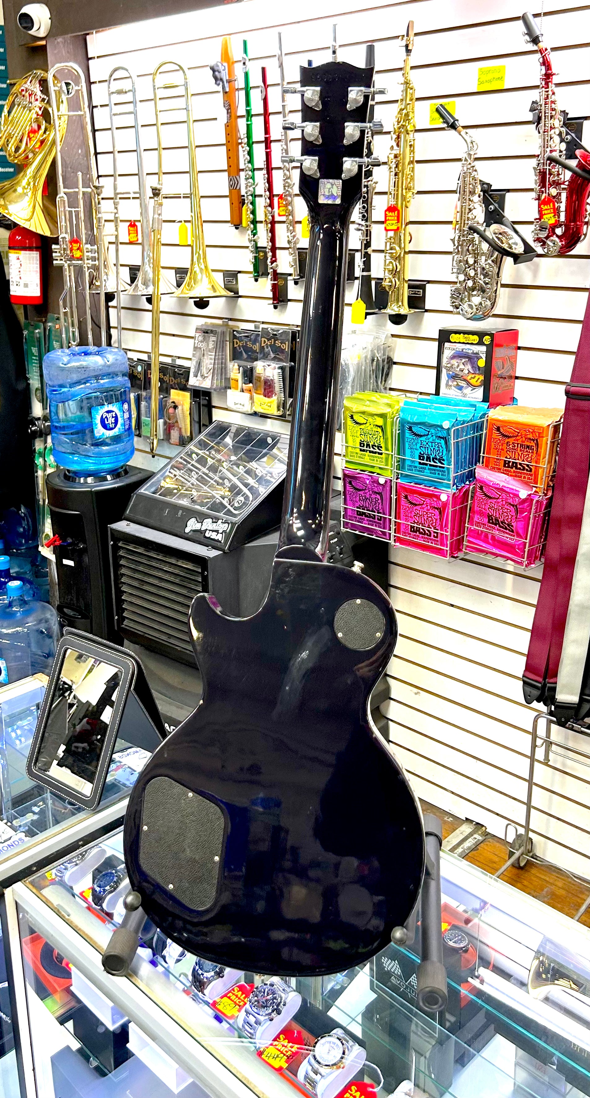 Black electric guitar on display in a music store with various instruments and products in the background.