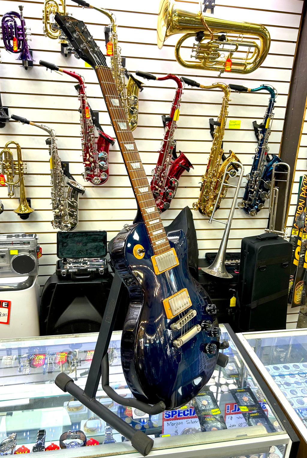 Blue electric Gibson Les Paul guitar on a stand in front of musical instruments in a store