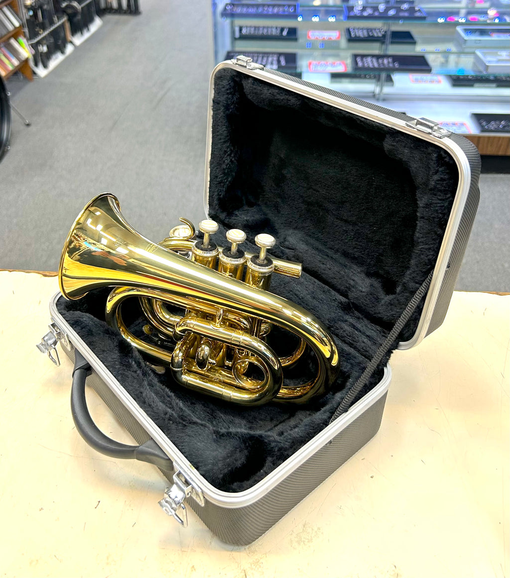 Gold travel pocket trumpet in a case on a table with a blurred background