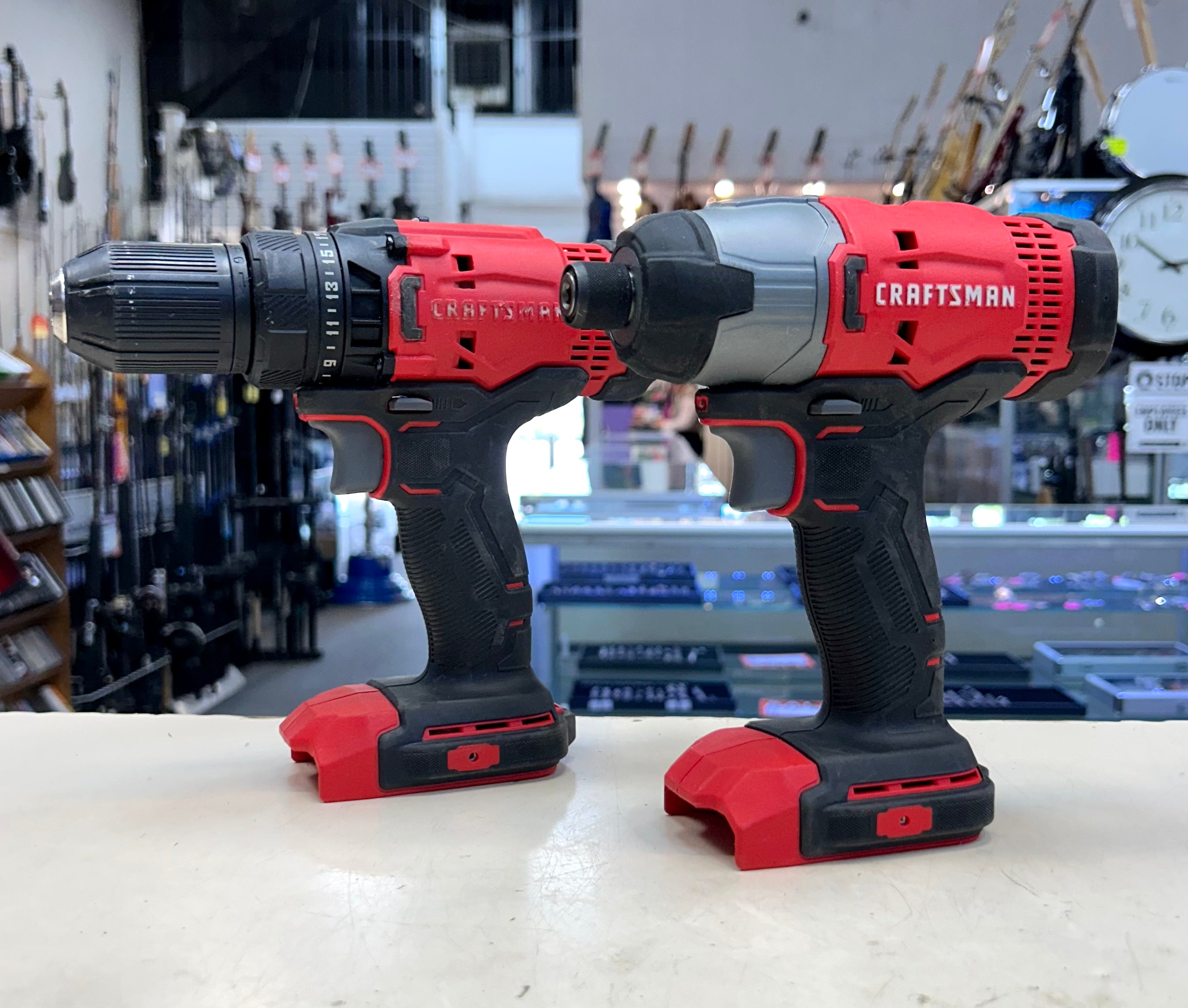 Two Craftsman power tools, a drill and an impact wrench, on a counter with a store background.