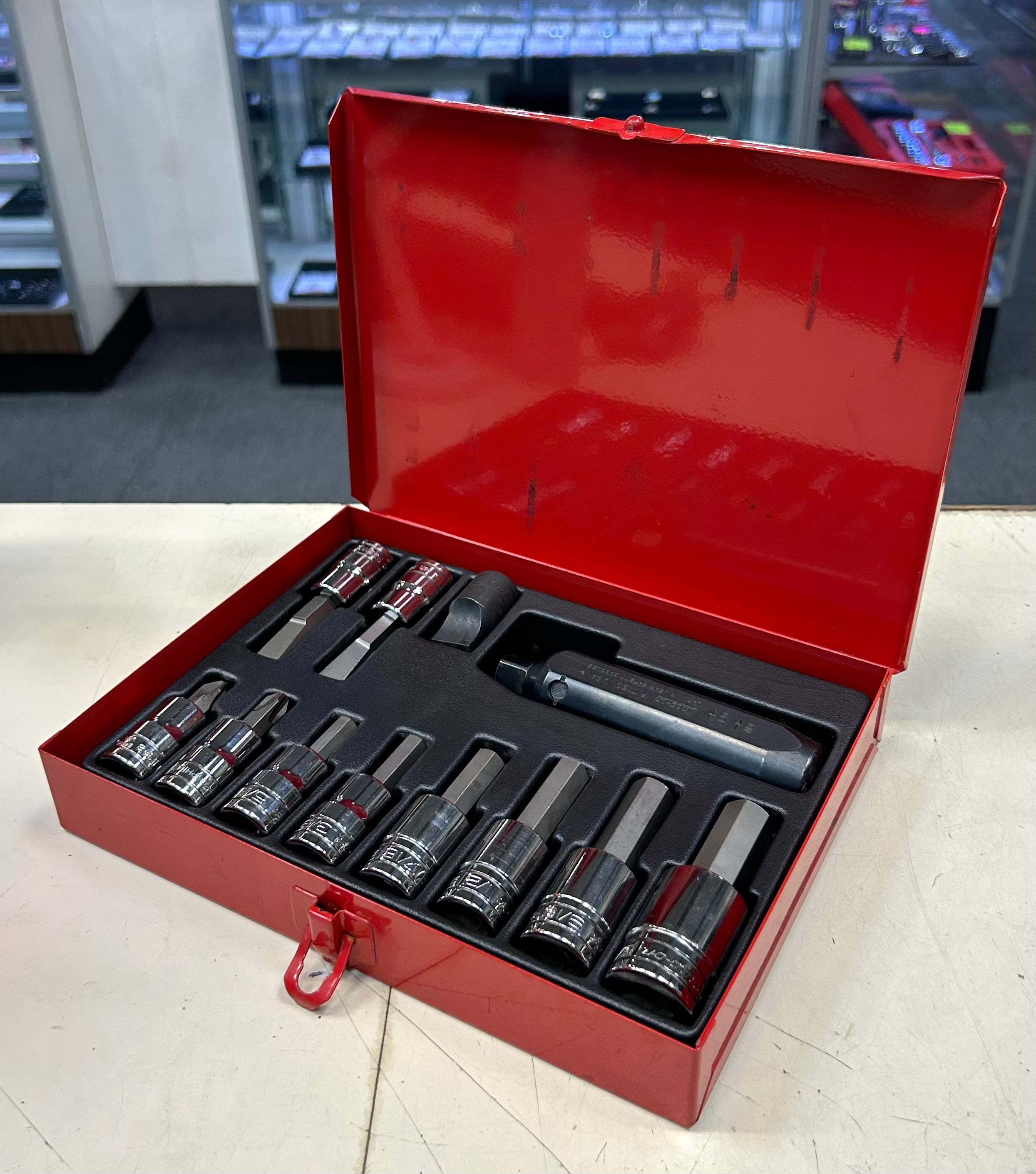 Open red tool box with various tools inside on a light surface.