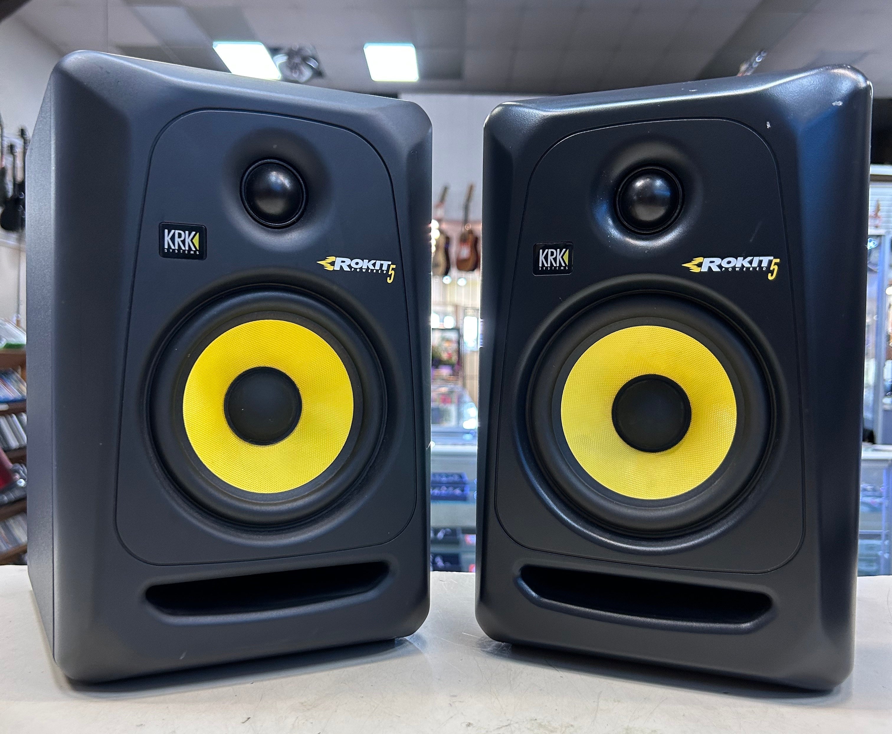 Pair of KRK ROKIT 5 studio monitors on a surface with a blurred background.