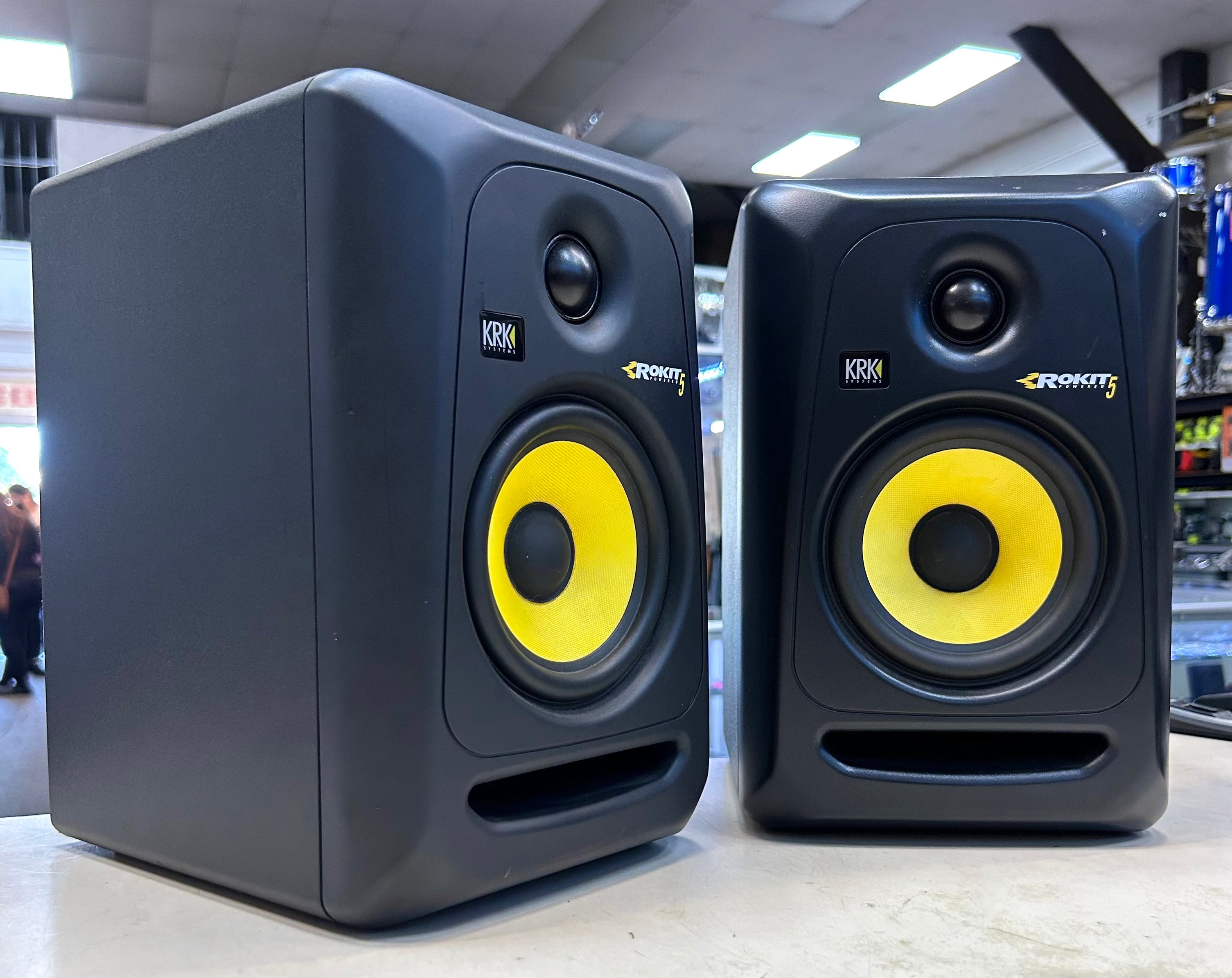 Two KRK studio monitors on a table with a blurred indoor background