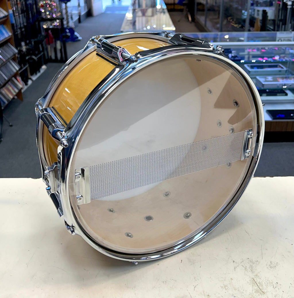 Snare drum with a yellow shell on a white surface, with a store interior in the background.