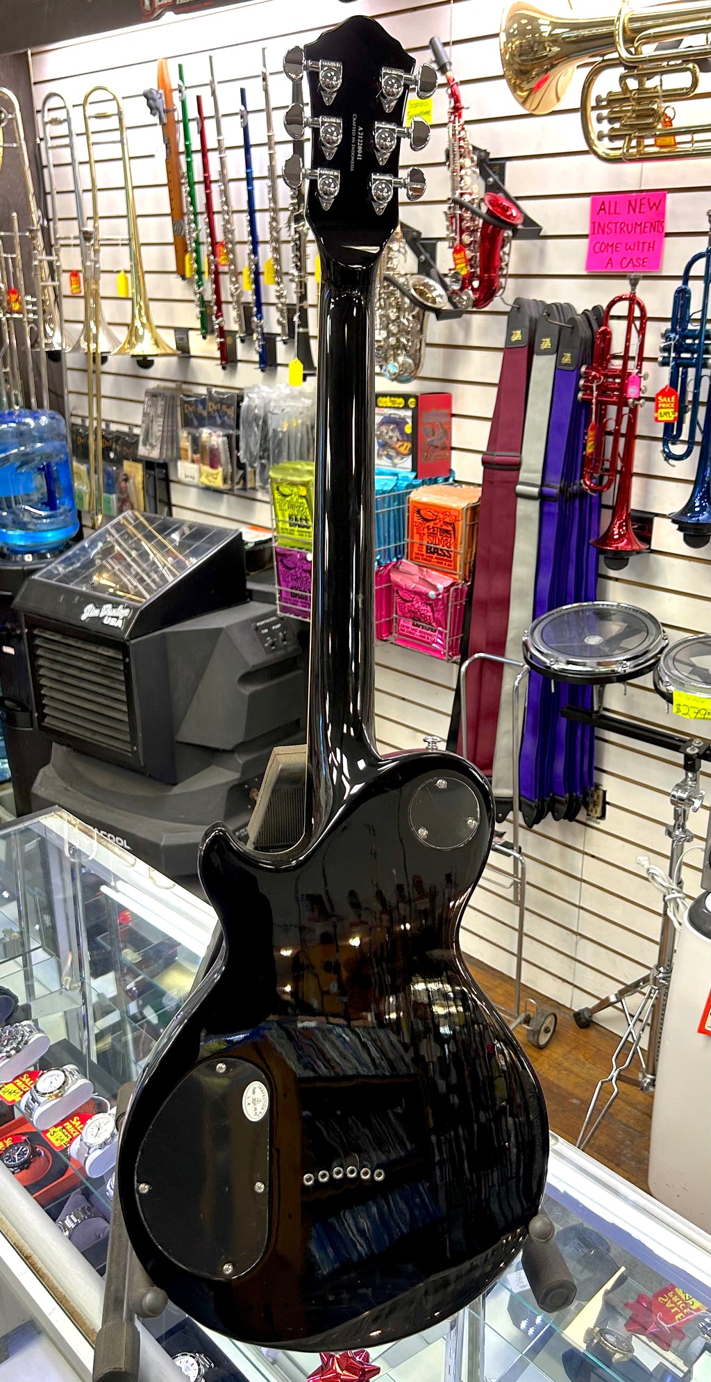 Black electric guitar in a case at a music store with various instruments in the background.