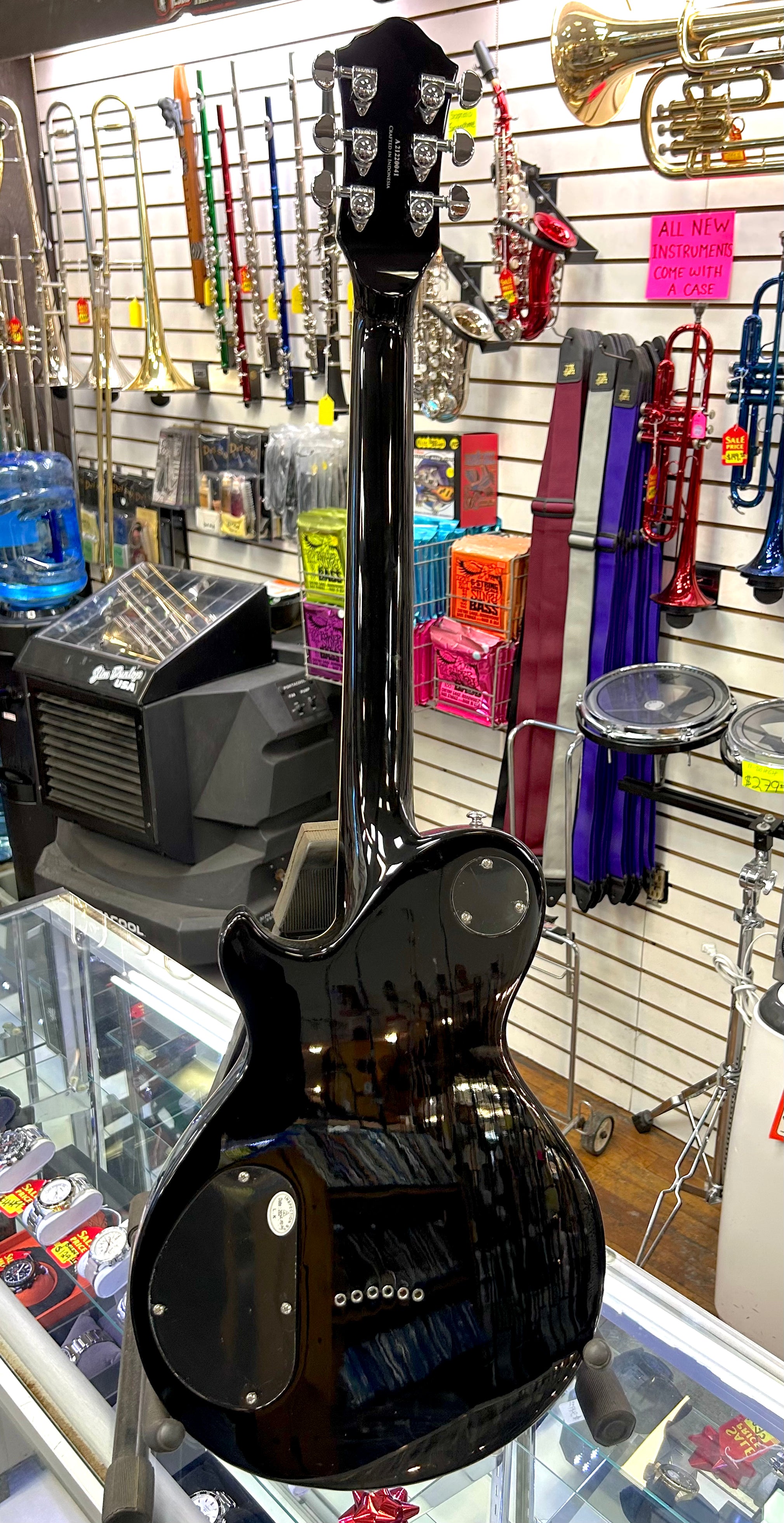 Black electric guitar in a case at a music store with various instruments in the background.