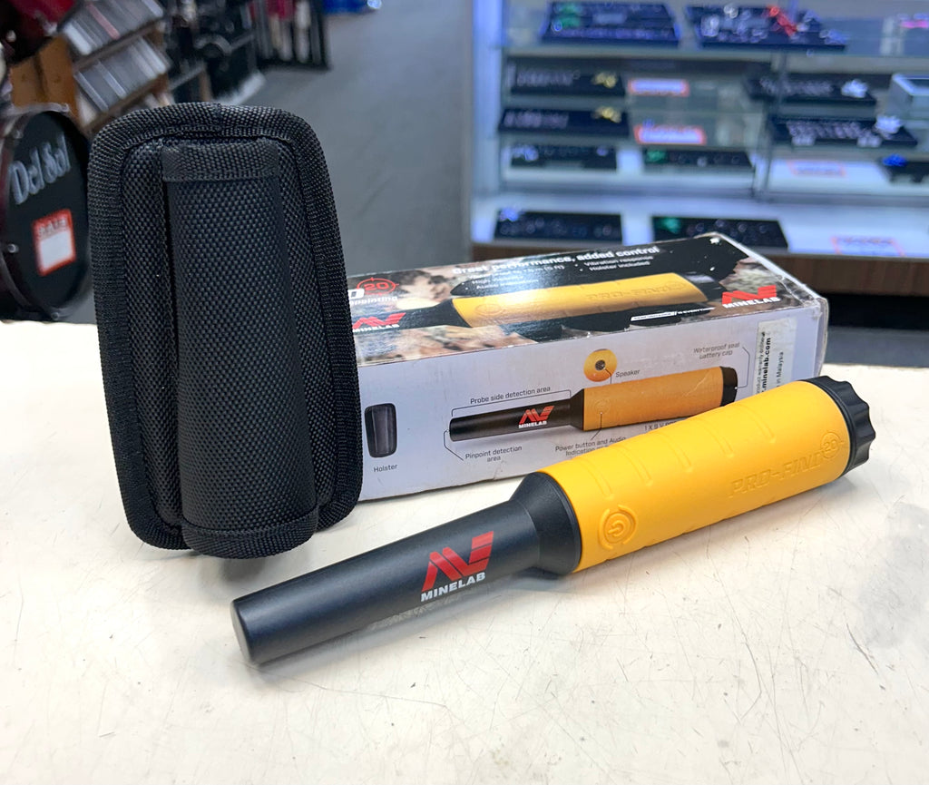 Metal detector with yellow and black handle and black carrying case on a table.