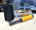Metal detector with yellow and black handle and black carrying case on a table.