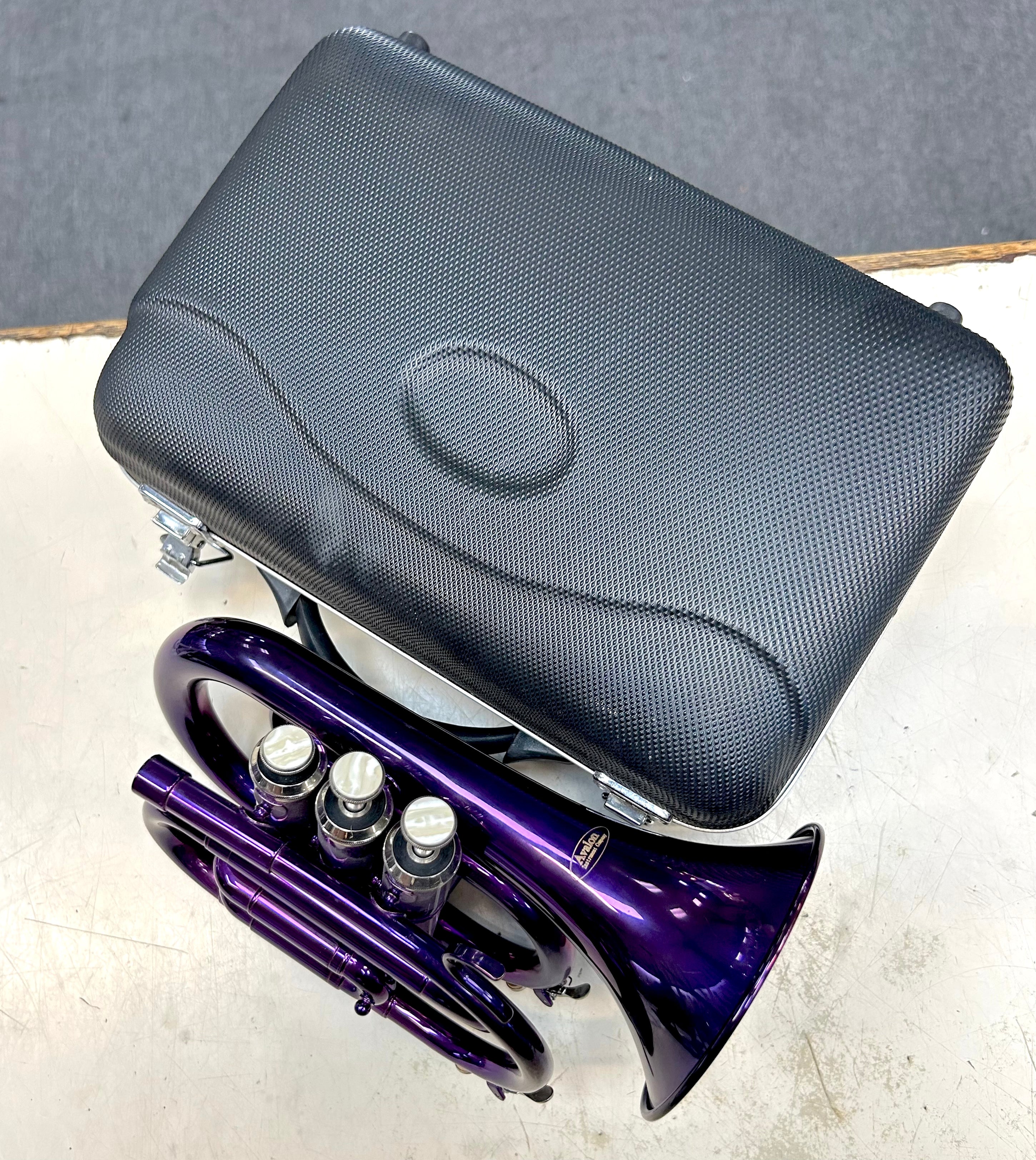 Purple beginner pocket trumpet with black case on a gray surface