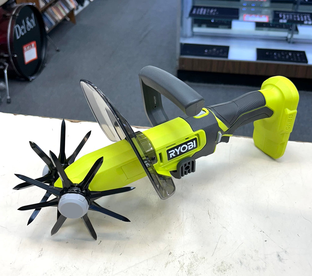 Ryobi power tool with attachments on a white surface, with a store interior in the background.
