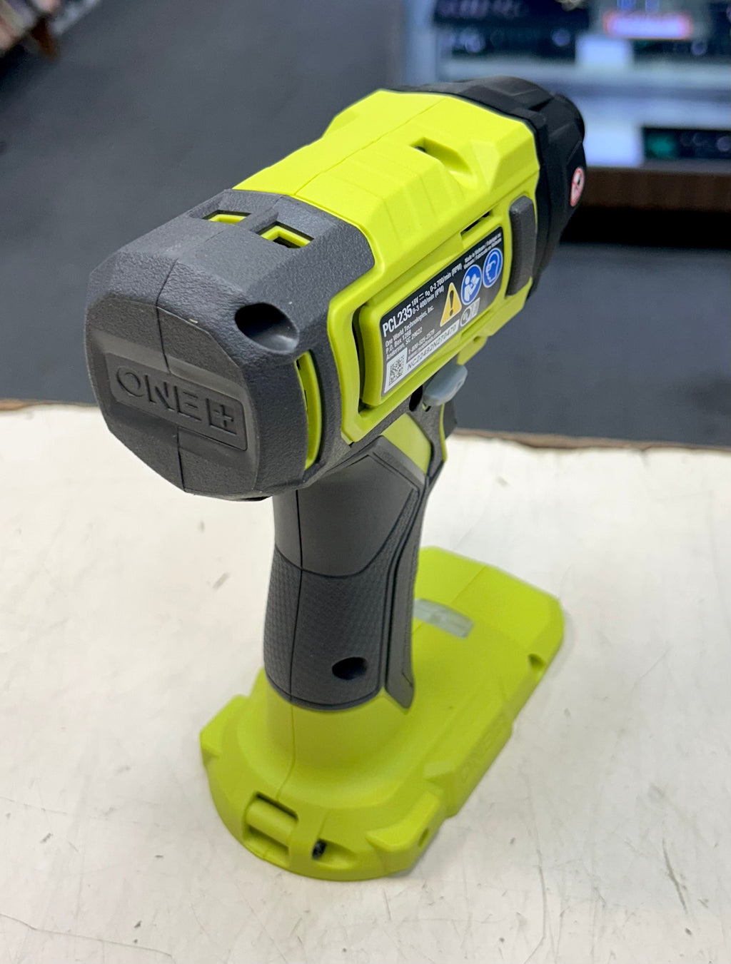 Green and gray Ryobi power tool on a white surface with a blurred background