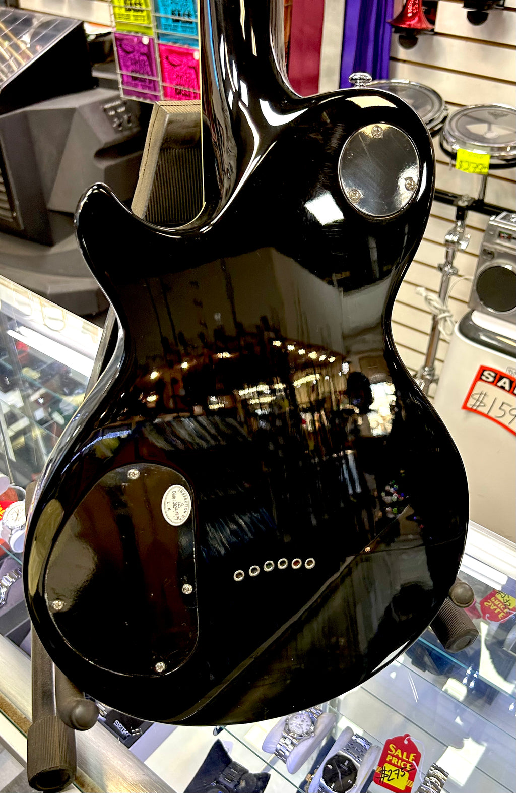 Black electric guitar on display in a store with reflective surface