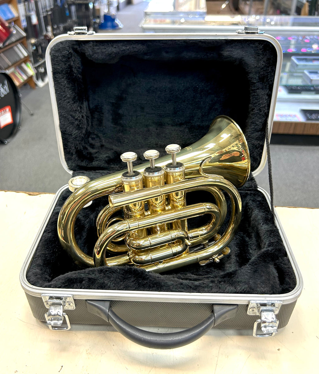 Gold pocket travel  trumpet in a black case on a table with a store background