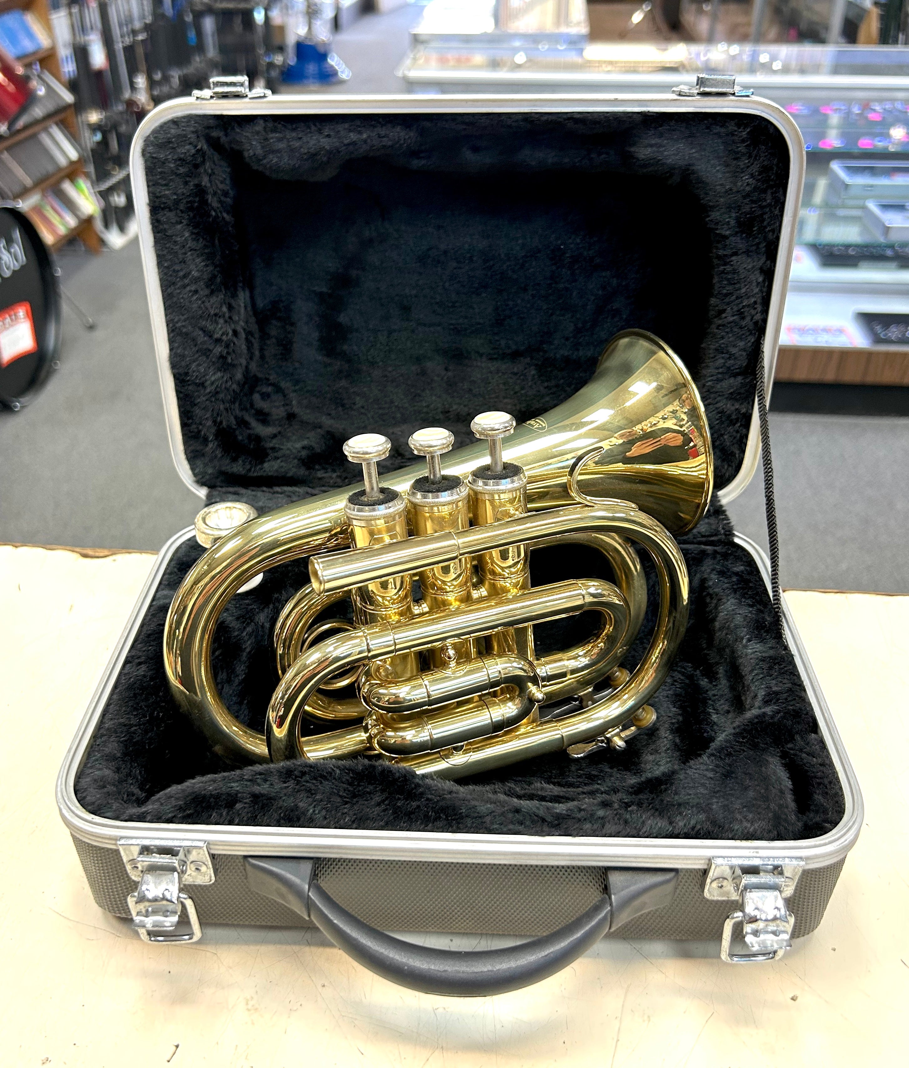 Gold pocket travel  trumpet in a black case on a table with a store background