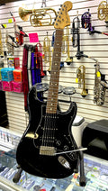 Black electric guitar on display with musical instruments in the background